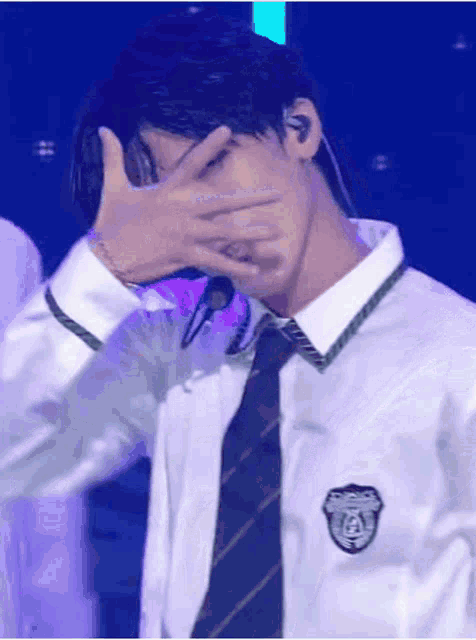 a man in a school uniform and tie is covering his face with his hands .