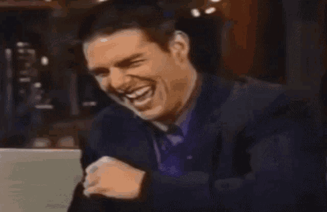 a man in a suit and tie is laughing while sitting on a couch .