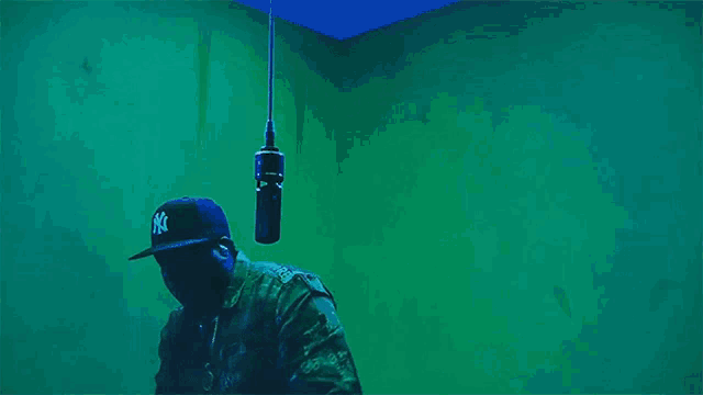 a man wearing a ny hat stands in front of a green wall