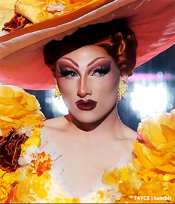 a drag queen wearing a hat and a dress with yellow flowers