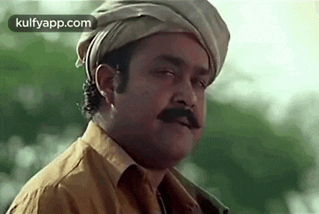a man with a mustache and a turban on his head is looking at the camera .