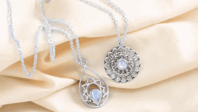 two necklaces are laying on a piece of fabric