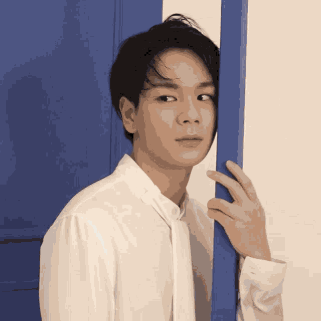 a young man in a white shirt is peeking out from behind a blue door
