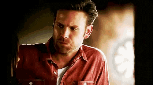 a man with a beard is wearing a red shirt and looking at the camera .