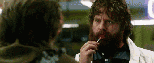 a man with a beard is eating a lollipop while another man watches .