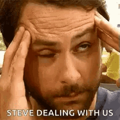 a man with a beard is holding his head with his hands while making a funny face .