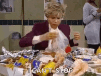 a woman is sitting at a table with a lot of food and eating a sandwich .
