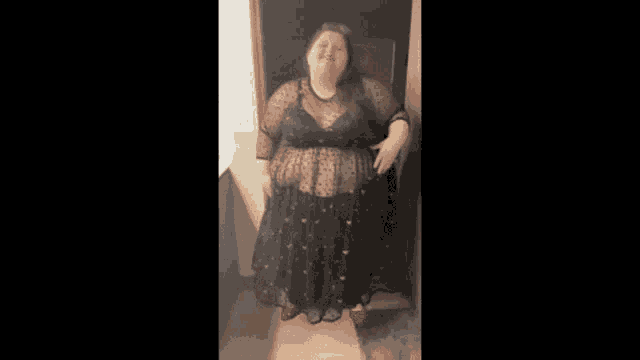 a woman is standing in a doorway wearing a black dress and bra .