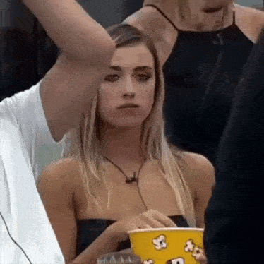 a woman is holding a bucket of popcorn while a man holds her arm .