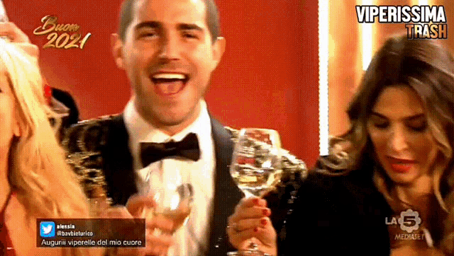 a man in a tuxedo holds a glass of wine in front of a screen that says buon 2021