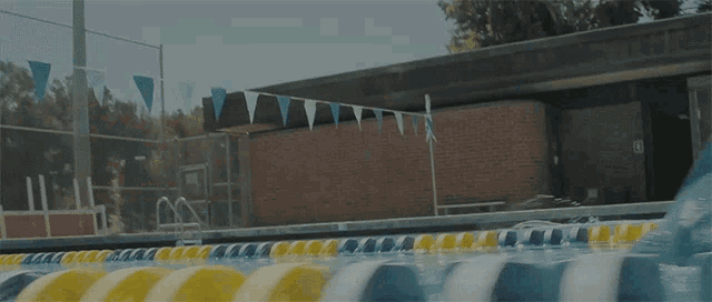 a swimming pool with a brick building in the background and flags hanging from the fence