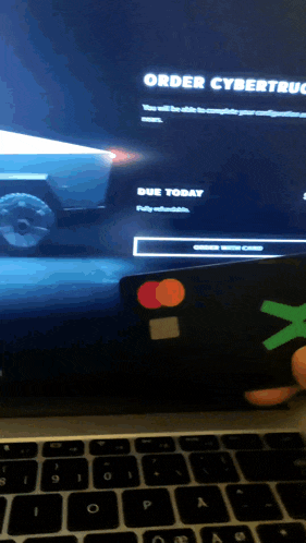 a person is holding a mastercard in front of a computer screen that says order cybertruck