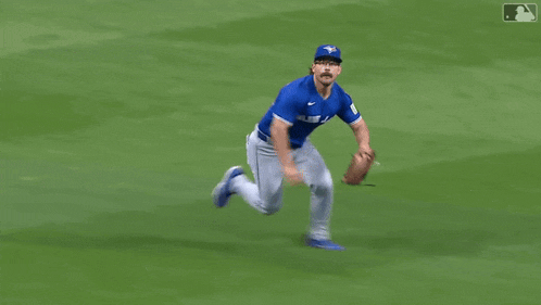 a baseball player in a blue jays uniform is trying to catch a ball .