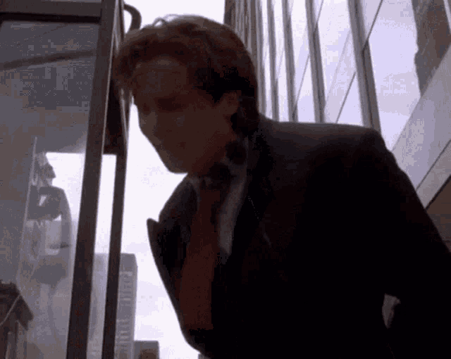 a man in a suit and red tie is standing in front of a phone booth