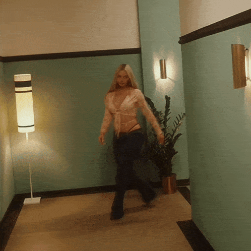 a woman walking down a hallway next to a plant and a lamp