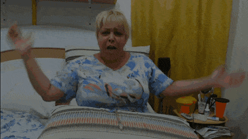 a woman in a blue and white shirt is sitting on a bed with a yellow curtain behind her