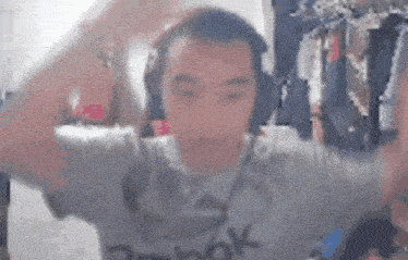 a man wearing headphones and a reebok shirt is dancing in front of a camera .