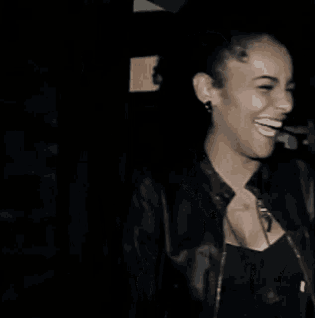 a woman wearing a black jacket and earrings smiles in the dark