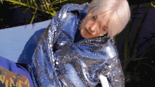 a woman wearing a blue sequined jacket is laying on a blue surface