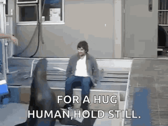 a man is sitting on a bench next to a seal that says `` for a hug human , hold still '' .