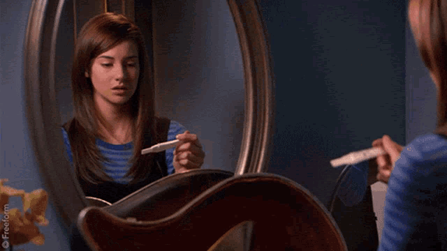 a woman holding a pregnancy test looking at herself in a mirror