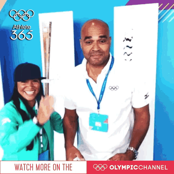 a man and a woman are posing for a picture in front of a sign that says olympic channel