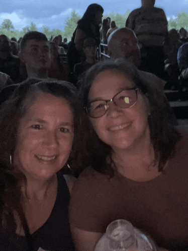 two women are posing for a picture while sitting in a crowded stadium