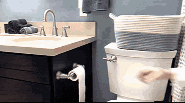 a person is using a toilet in a bathroom with a basket on top of it