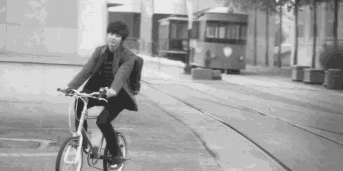 a black and white photo of a man riding a bike on a street