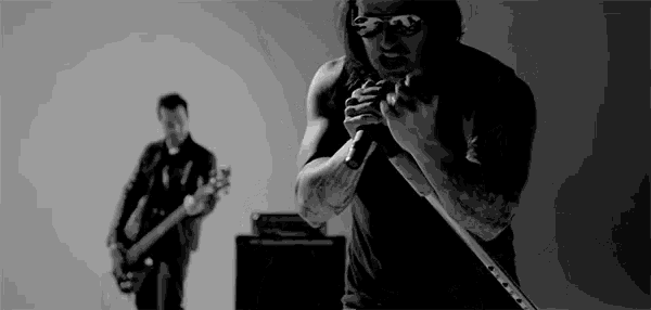 a man is singing into a microphone in a black and white photo while another man plays a guitar .