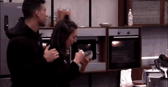 a man and a woman are in a kitchen looking into a microwave