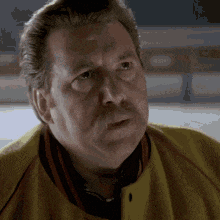 a man with a beard wearing a yellow jacket looks at the camera