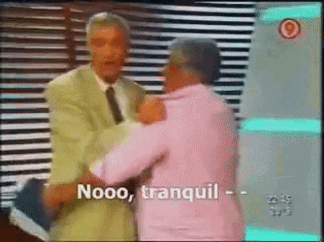 a man in a suit and tie is hugging another man in a pink shirt with the words nooo tranquil written on the screen