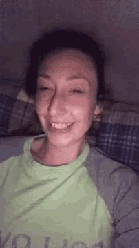 a woman in a green shirt is smiling while laying on a bed with her eyes closed .