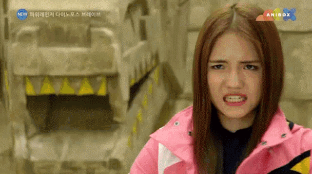 a girl in a pink jacket is making a funny face in front of an anibox sign
