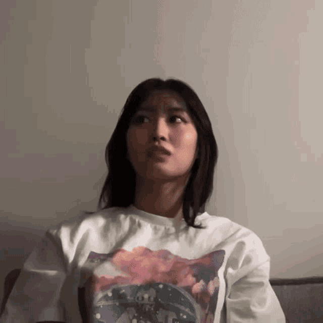 a woman is sitting on a couch wearing a white t-shirt with a picture on it .