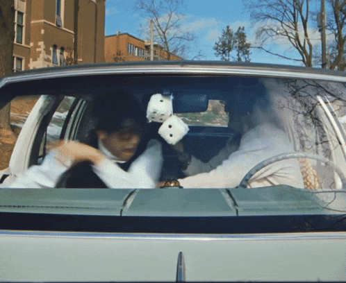 a man and woman in a car with dice in the rear view mirror