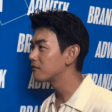a man in a white shirt stands in front of a blue wall that says brand