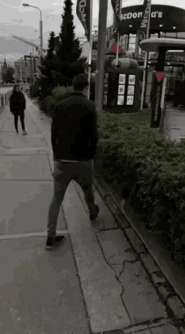 a man walking down a sidewalk in front of a mcdonald 's restaurant