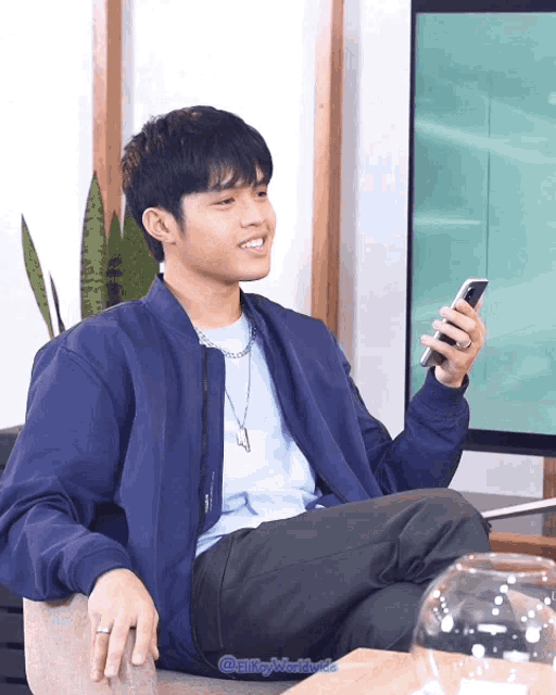 a man in a blue jacket is sitting in a chair looking at his cell phone