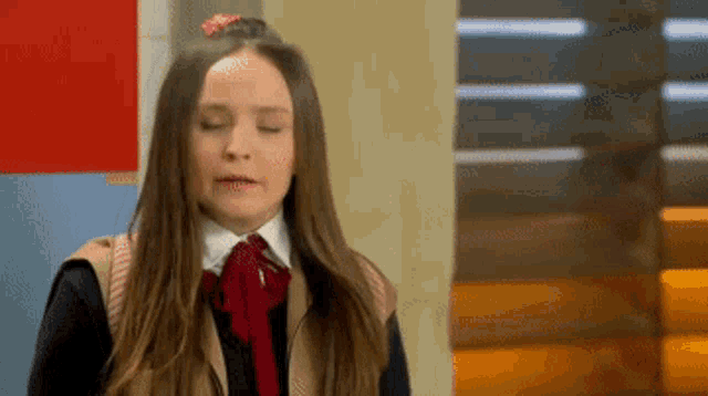 a girl in a school uniform with her eyes closed and a bow in her hair .