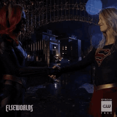 a woman in a superman costume shakes hands with a woman in a batman costume ..