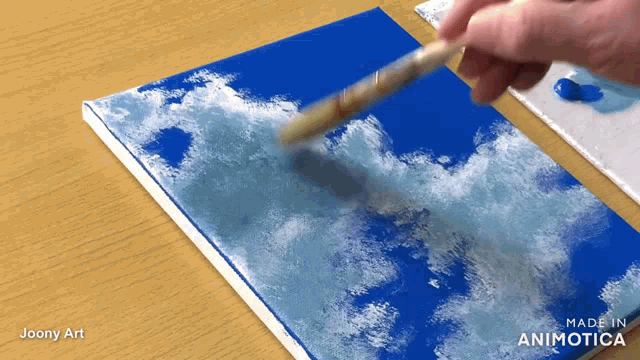 a person is painting a blue sky with white clouds on a canvas with the words made in animatica on the bottom
