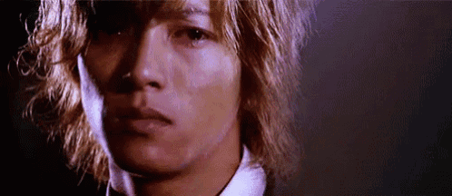 a close up of a man 's face with long blonde hair and a white shirt and tie .