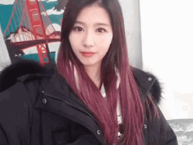 a woman with purple hair is wearing a black jacket with a fur hood and taking a selfie .
