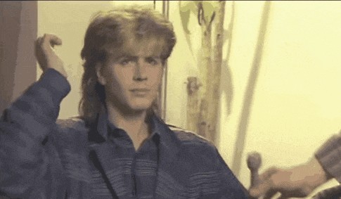 a man with a mullet is standing in front of a wall .