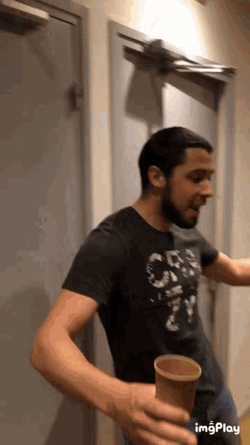 a man with a beard is holding a cup and wearing a black shirt that says ' crew city ' on it