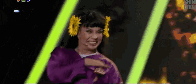 a woman in a purple dress with yellow flowers in her hair is dancing on a stage .