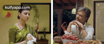 a woman is holding a napkin next to a man sitting at a table with a bowl of fruit .