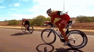 a man is riding a bike down a road while another man is riding a bike behind him .